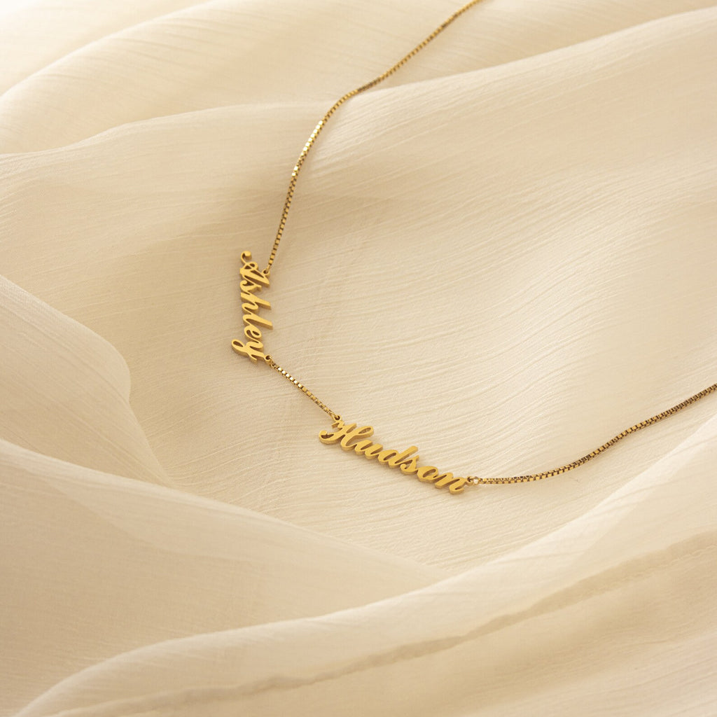 Carrie Multiple Name Necklace in Box Chain, shown with "Ashley" and "Hudson" on a cream sheer fabric background—perfect personalized jewelry for a unique touch.