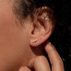 Close-up of an ear wearing Tiny Pearl Bar Studs, a gold everyday earring featuring three freshwater pearls, with a hand gently touching the ear.