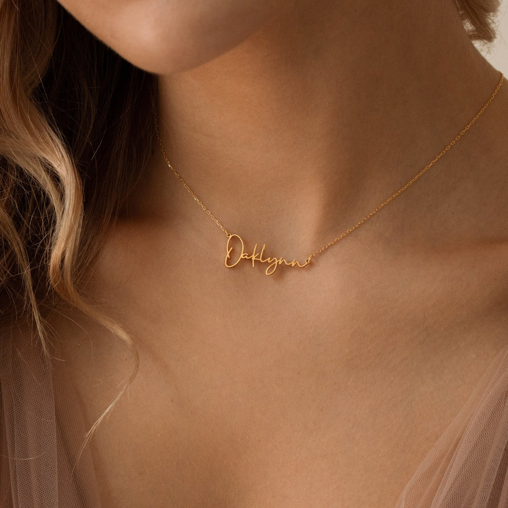 Close-up of a woman wearing the Tiny Summer Name Necklace personalized with "Deklyn" in delicate gold cursive script.