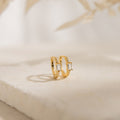 The Natalie Pave Huggies are dainty hoop earrings with rectangular clear gemstones, reminiscent of baguette diamond earrings, displayed on a light textured surface.