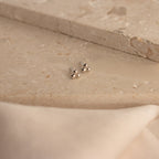 Trio Sphere Studs in silver are displayed on a beige stone surface with soft fabric in front—ideal for stacking or unique piercings.