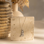 Custom Pet Portrait Necklace shown on a textured stone slab with beige decor and dried flowers—an elegant pendant amulet that celebrates your beloved pet.