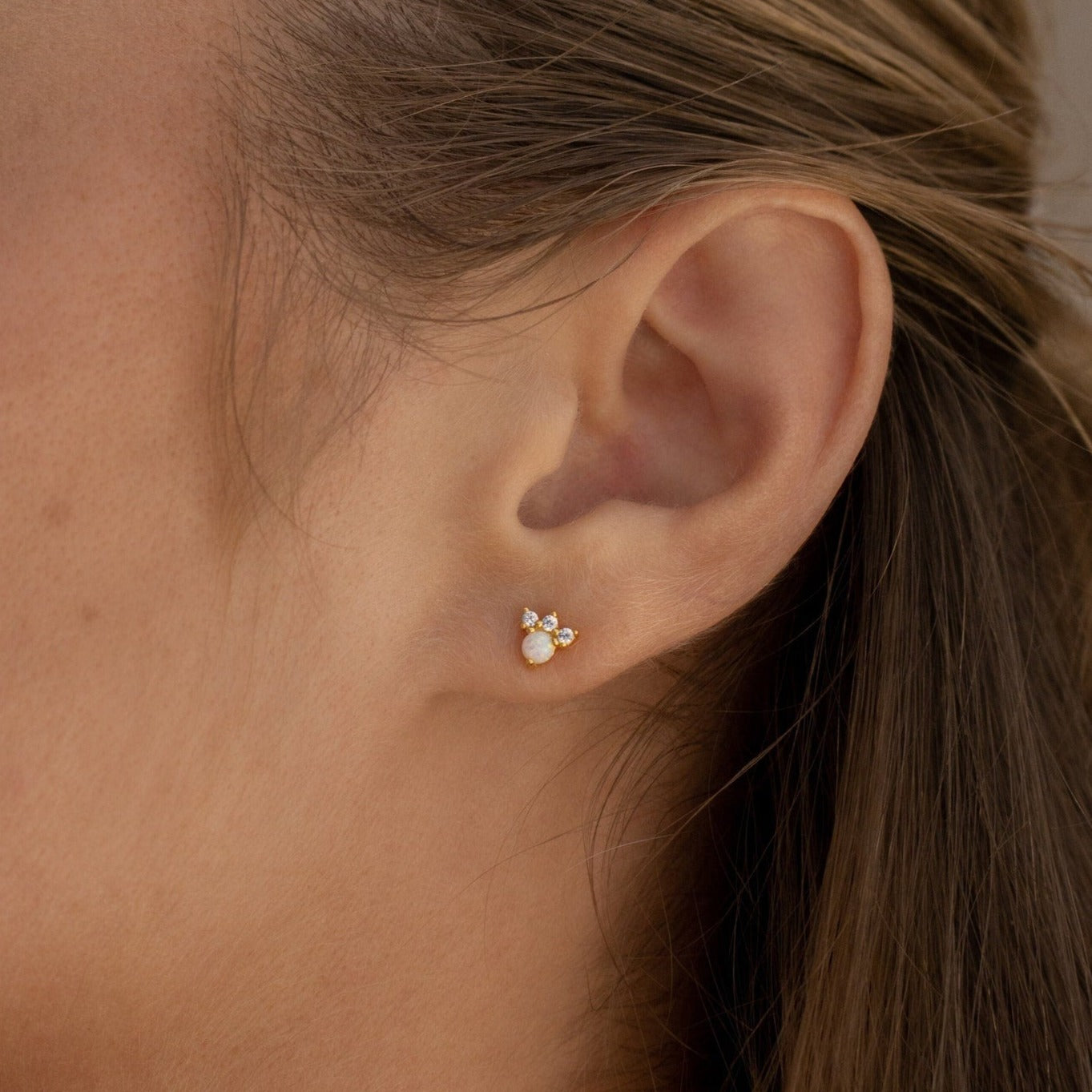 Close-up of a woman's ear wearing Jackie Opal Studs—dainty gold and white opal earrings, perfect for those who love subtle elegance.