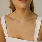 A woman wears a white top and the Pave Sideways Initial Necklace, featuring a delicate diamond letter E pendant.