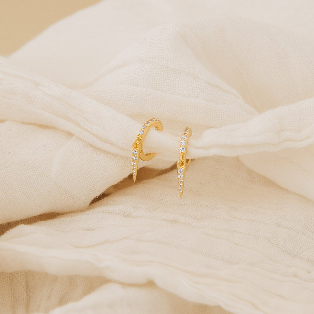 Quinn Pave Dagger Huggies are shown resting on soft, cream-colored fabric, highlighting their delicate diamond accents.