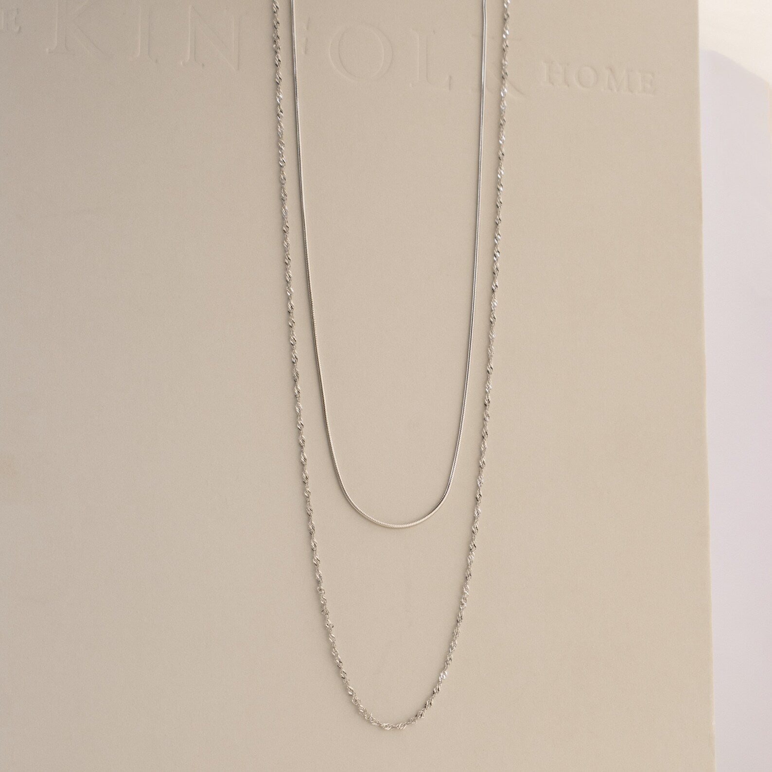 The Monet Duo Chain, with a sleek snake and elegant Singapore chain design, is displayed on a light beige background.