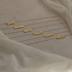 Six Grace Name Necklaces displayed on a beige fabric background, each featuring names in elegant cursive script. Perfect as custom nameplate jewelry for a unique, personal touch.