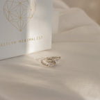 Two Aster Pave Twisted Hoops in silver sit on cream fabric next to a white box labeled AITLYN MINIMALIST—ideal for anyone who loves dainty earrings.
