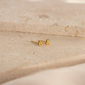 The Trio Sphere Studs feature a small gold three-dot cluster design, displayed on a beige stone surface—ideal for creating an elegant earring stack or accenting alternative piercings.