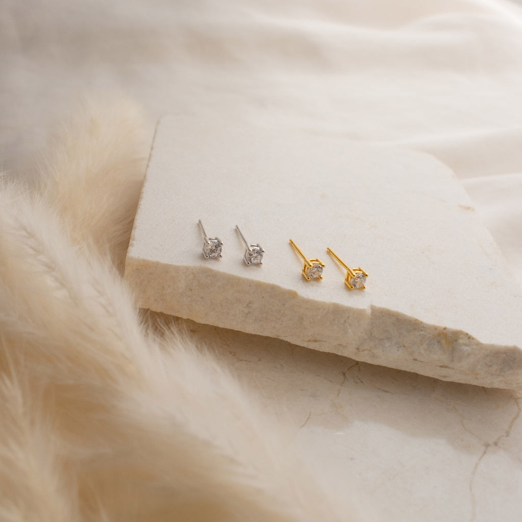 Booker Classic Diamond Studs—two pairs, in silver and gold, shown on a stone slab with a soft backdrop. Perfect everyday earrings for effortless style.