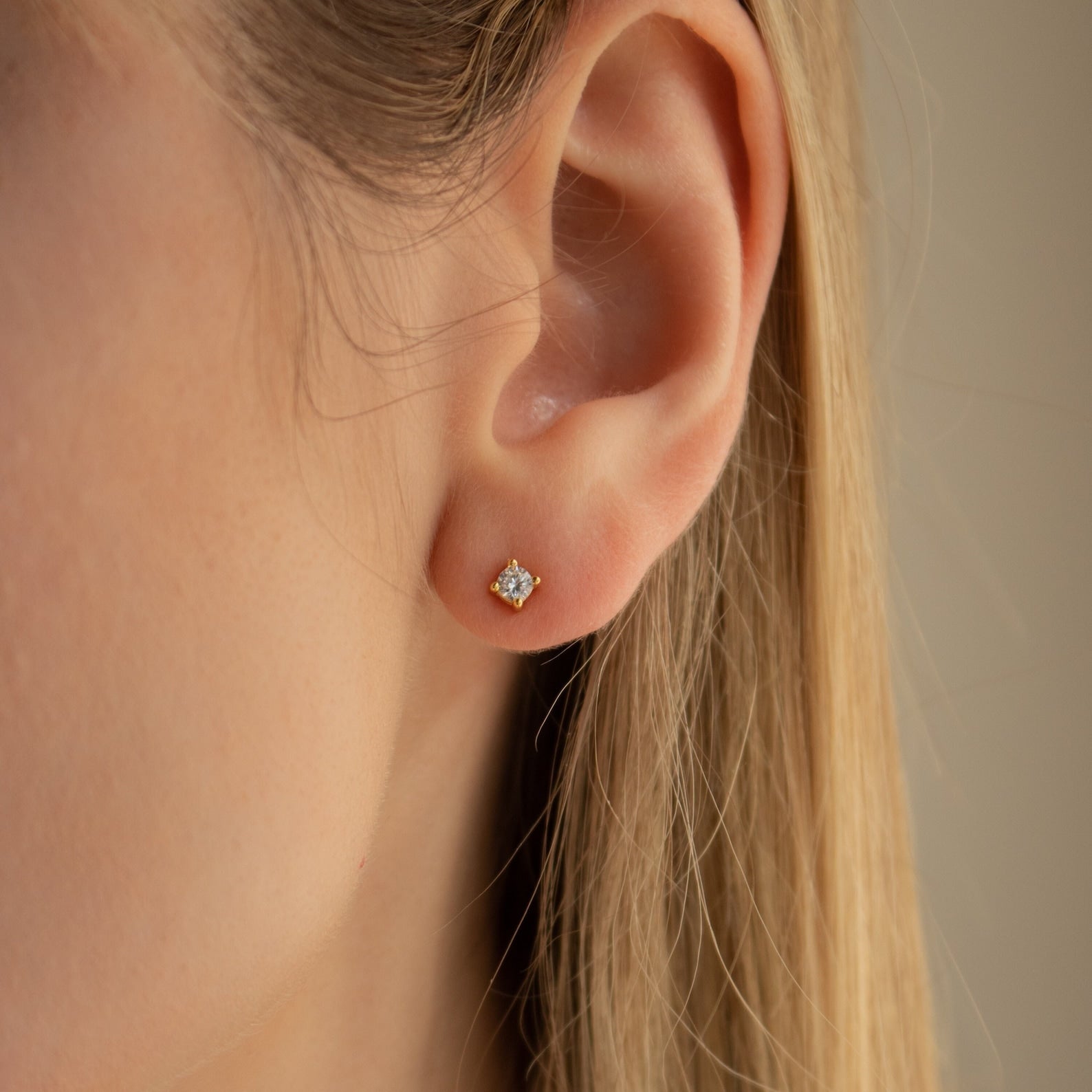 Close-up of a womans ear adorned with Booker Classic Diamond Studs in a gold setting. Her light skin and straight, blonde hair appear softly blurred against a neutral background.