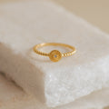 The Eden Sun Ring features a delicate boho-chic sunburst design with textured gold and a small central stone, displayed on a marble surface.