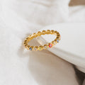 The Rainbow Evil Eye Ring features colorful enamel charms and small crystals, shown on soft white fabric. This vibrant jewelry piece is a stylish, unique lucky charm ring perfect for any occasion.
