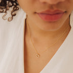 A person wearing the Forever Pave Heart Necklace, featuring a gold chain and small heart-shaped pendant, dressed in a white top.
