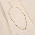 The Santorini Turquoise Choker features a gold chain adorned with small turquoise drops, shown on a light textured background.