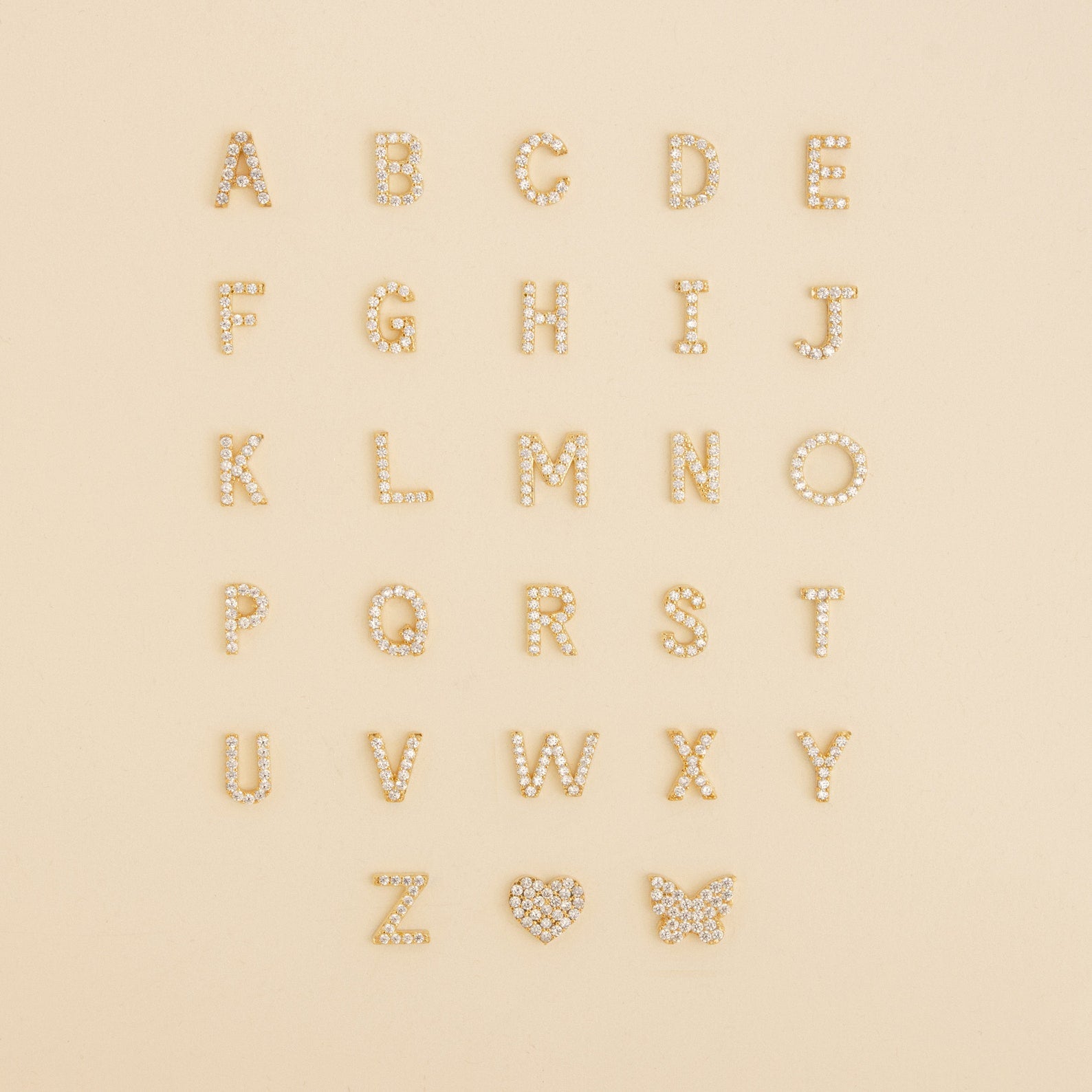 Gold and pearl letters A-Z arranged in rows, with a heart and butterfly at the bottom right—perfect inspiration for the Dangling Pave Initial Necklace, an elegant and thoughtful gift for women.