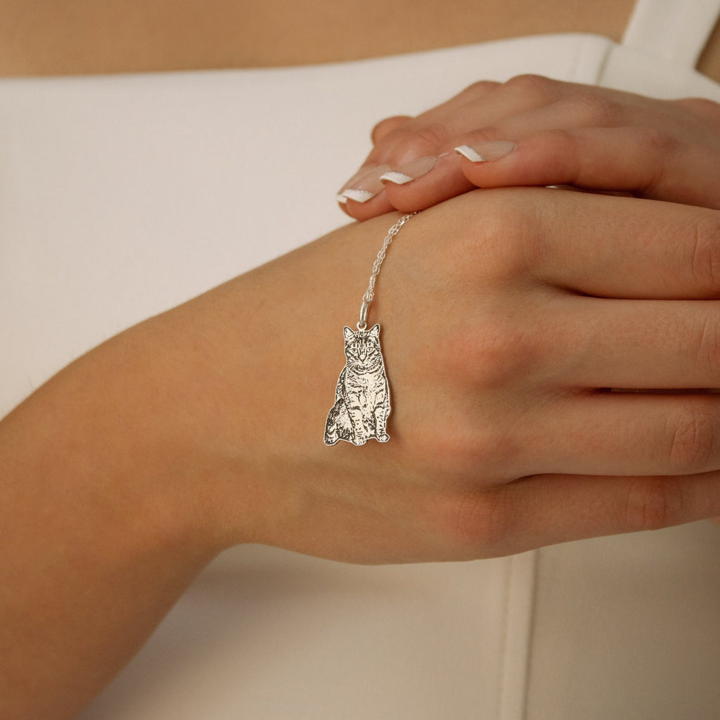 A Custom Pet Portrait Necklace with a cat-shaped pendant, shown elegantly on a woman's lightly manicured hand.