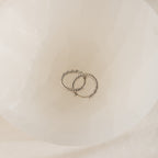 Two Aster Pave Twisted Hoops, crafted in silver and elegantly intertwined, are displayed inside a white, translucent bowl.