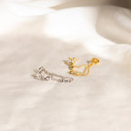 Genesis Chain Earrings in gold and silver, adorned with gemstones, make a stunning statement and are elegantly displayed on a soft white fabric background.