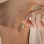A gold chain necklace with a white oval pendant featuring the letter 'R' in gold lettering with the pendant being held to the camera by a model.