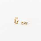 The Glacier Baguette Huggies feature gold hoops with geometric shapes and rectangular clear stones for minimalistic sparkle, elegantly shown on a white background.