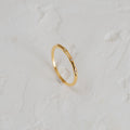 The Juliet Diamond Ring, a minimalist piece with three small diamonds, shines elegantly on a white textured surface.