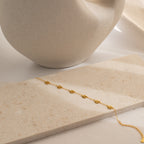 The Flower Child Bracelet, a delicate gold piece with star-shaped charms, displayed on beige stone near a ceramic vase, brings a cottage-core touch to your style.