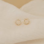 Helen Diamond Sun Studs—gold circular minimal earrings with small clear stones—are displayed on soft beige fabric. These dainty diamond studs add a subtle sparkle to any look.