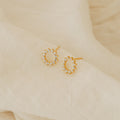 Helen Diamond Sun Studs with small clear stones, shown on soft cream fabric—perfect minimal earrings for a subtle, sparkling touch.