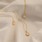 Three Initial Pendant Necklaces in 18K Gold, each featuring a round charm engraved with a C, M, or K, are displayed on soft fabric.