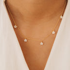 The Nanala Diamond Flower Necklace, featuring delicate flower-shaped charms, sparkles on a person in a white top, bringing an elegant touch to any outfit.