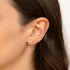 Close-up of a woman's ear wearing three Maeve Opal Studs—small, round gemstone earrings featuring colorful opals for a subtle yet striking statement look.
