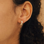 Close-up of a person's ear wearing Glacier Baguette Huggies—minimalist gold earrings featuring geometric shapes with clear and yellow stones.