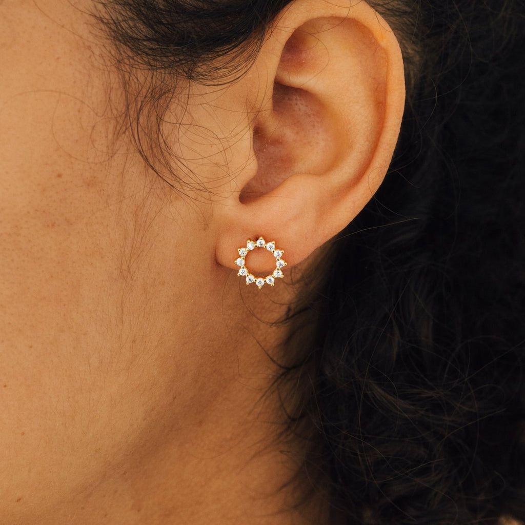 A close-up of an ear wearing the Helen Diamond Sun Studs—delicate gold earrings featuring sparkling diamond accents.