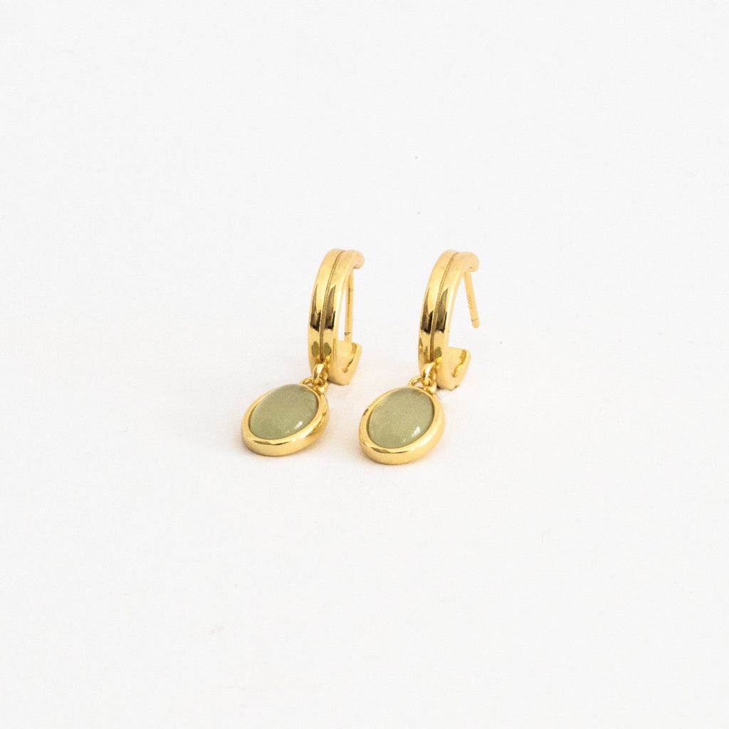 Pair of gold hoop earrings with oval jade gemstone drop pendants displayed on a clean white surface, showcasing a modern and dainty jewelry style.