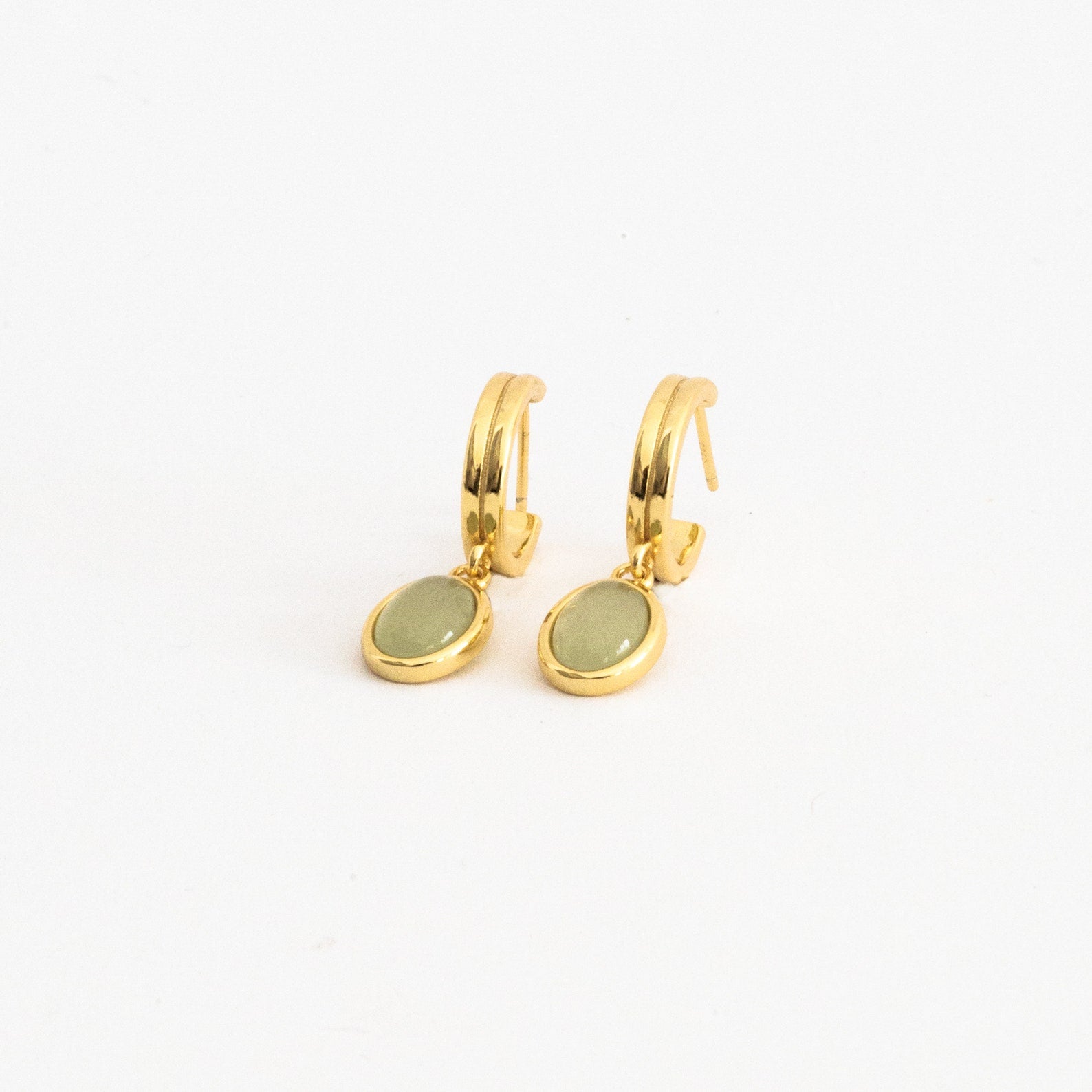 Pair of gold hoop earrings with oval jade gemstone drop pendants displayed on a clean white surface, showcasing a modern and dainty jewelry style.