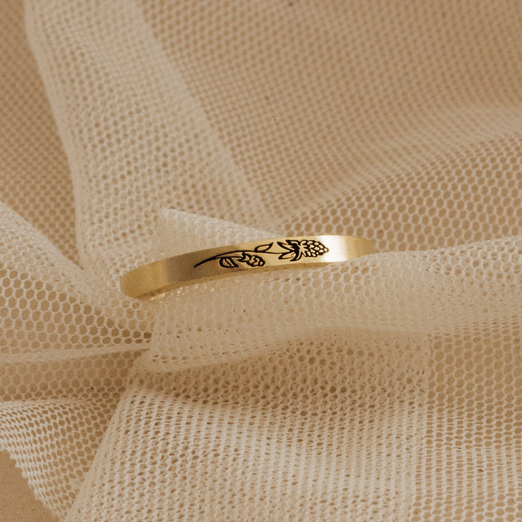 The Stacking Flower Band, featuring a delicate floral engraving, rests on soft beige mesh fabric, highlighting the elegance of botanical-inspired jewelry.