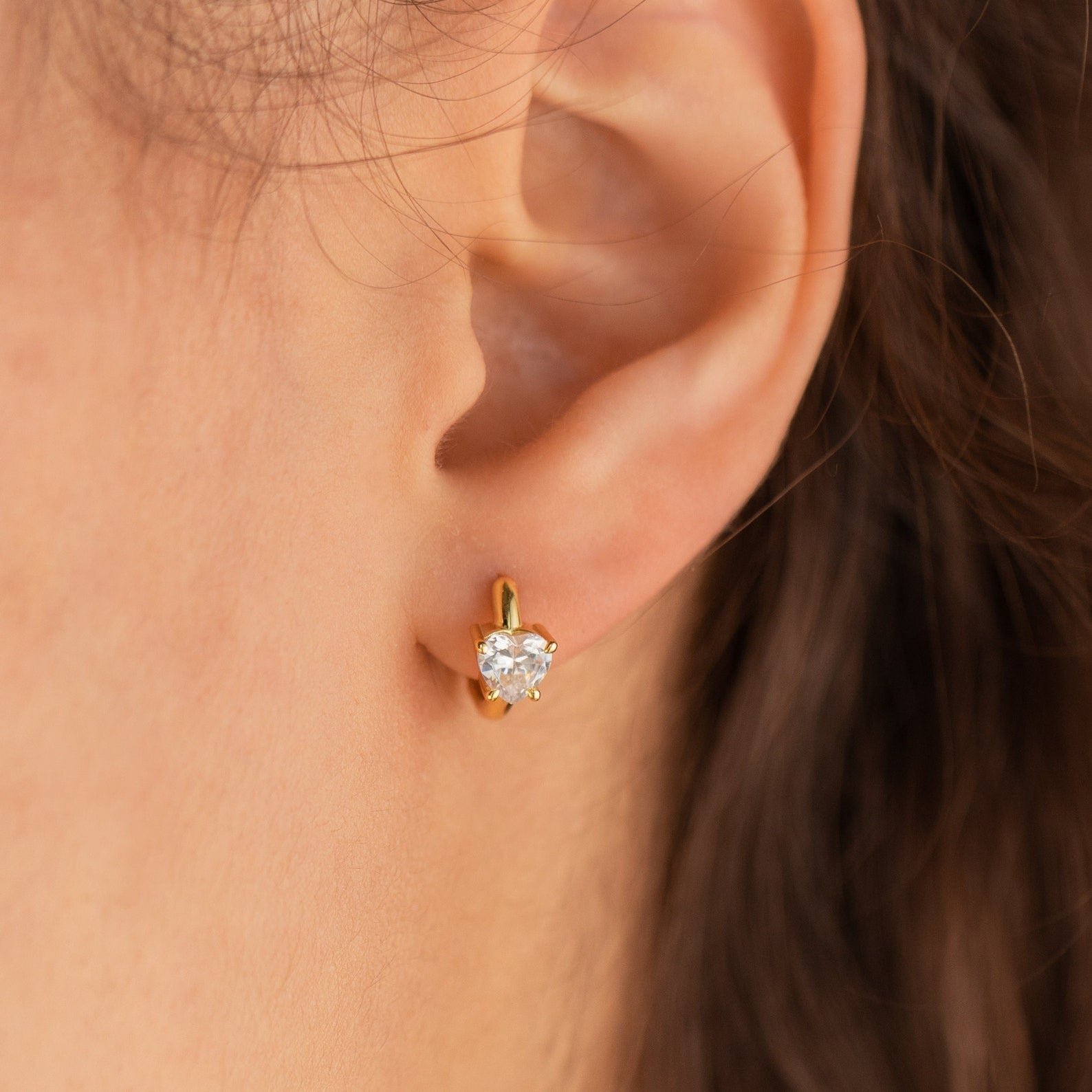 Close-up of an ear with a gold stud earring featuring a round clear gemstone, perfect as a gift or paired with the Diamond Heart Huggies for an elegant, layered look.