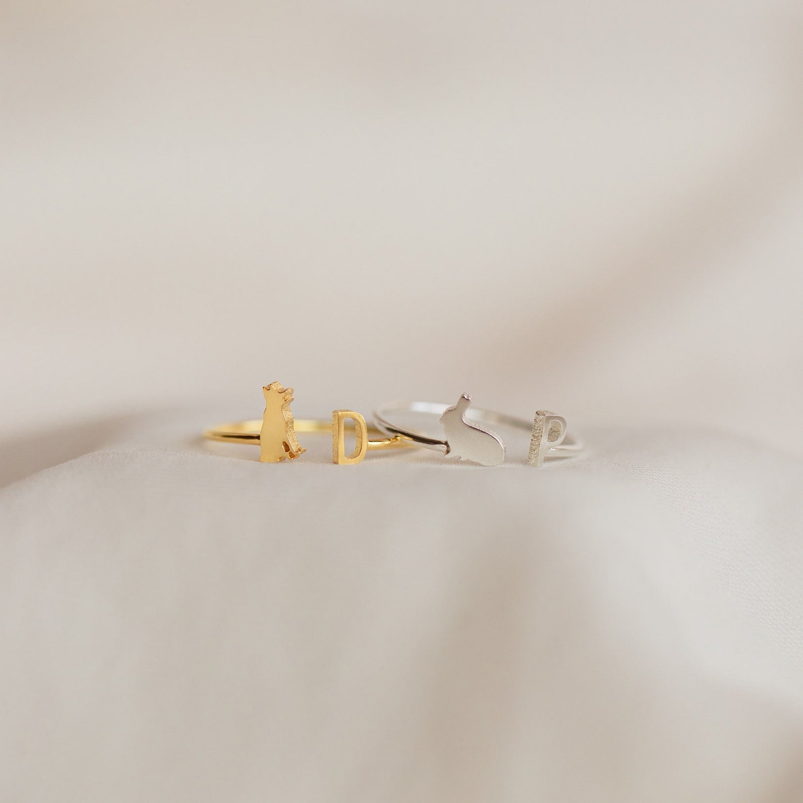 The Duo Pet Initial Ring features two minimalist rings on fabric: a gold bear with initial D and a silver cat with initial P—ideal as personalized pet jewelry or a custom gift for pet lovers.