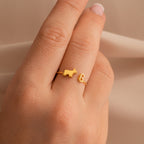 A Duo Pet Initial Ring featuring a gold cat and letter G design on a finger, close-up on a neutral background—the ideal personalized jewelry for animal lovers.