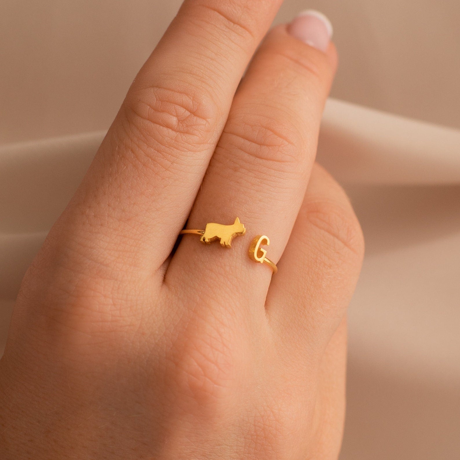 A Duo Pet Initial Ring featuring a gold cat and letter G design on a finger, close-up on a neutral background—the ideal personalized jewelry for animal lovers.