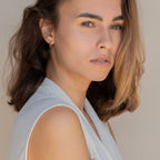 A woman with brown hair wearing a white shirt showcases the McKenna Abstract Hoops, everyday earrings with an organic shape.