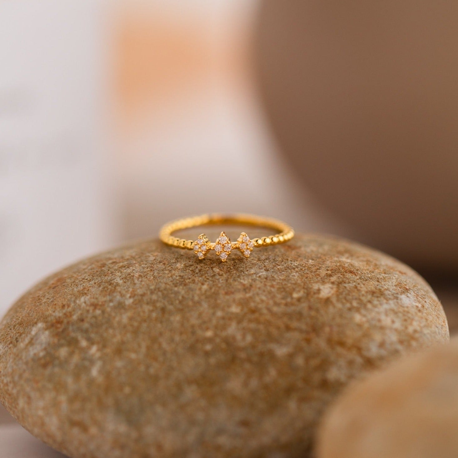 The Jasmine Beaded Diamond Ring, a delicate gold vintage piece featuring three small diamonds, rests on a smooth, round stone.