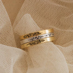 The Stacking Flower Band, an engraved gold and silver ring with a floral design, rests on textured cream fabric—an ideal piece for lovers of botanical jewelry.