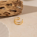 The Everly Thin Duo Band sits on a beige textured surface with a dried natural accent in the background, showcasing its elegant double-band design—ideal as an adjustable stacking ring.