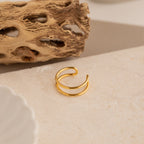 The Everly Thin Duo Band sits on a beige textured surface with a dried natural accent in the background, showcasing its elegant double-band design—ideal as an adjustable stacking ring.