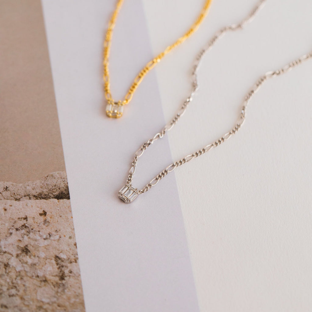 Square Diamond Figaro Necklaces, crafted in gold and silver with small square pendants—some set with sparkling baguette diamonds—are displayed on a neutral background.