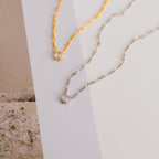 Square Diamond Figaro Necklaces, crafted in gold and silver with small square pendants—some set with sparkling baguette diamonds—are displayed on a neutral background.