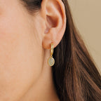 Side profile of a model wearing gold hoop earrings with a small oval jade gemstone pendant, styled as delicate everyday jewelry with a natural look.