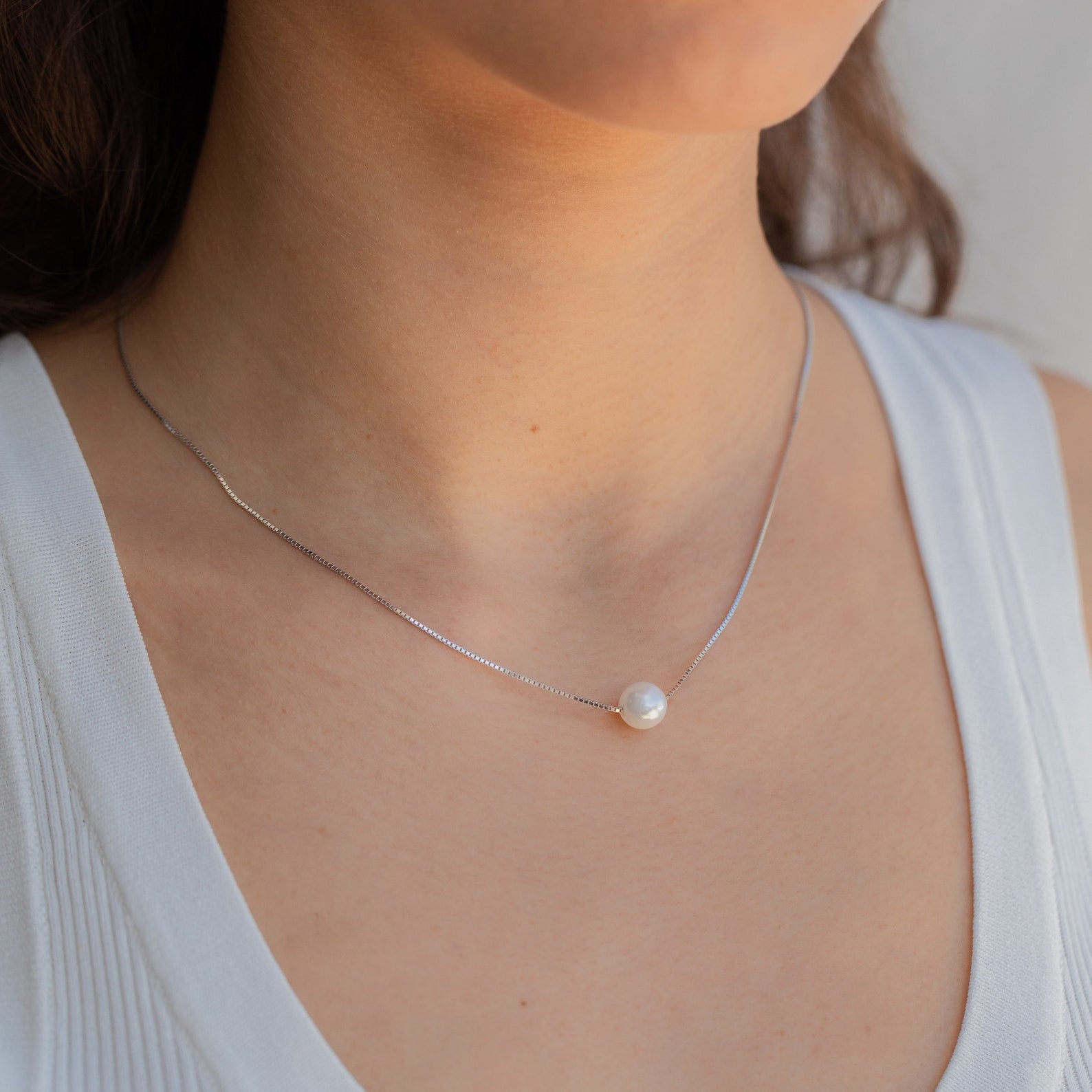 A woman wearing a white top and the Kennedy Pearl Necklace, ideal for fans of minimalist jewelry.
